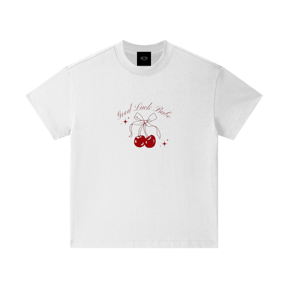 A white short-sleeve crewneck t-shirt with a graphic on the chest featuring red cherries tied with a bow, red sparkles, and the text 'You A F*ck B*tch' in a cursive font. A black neck label with the brand 'SCH' is visible inside the collar.